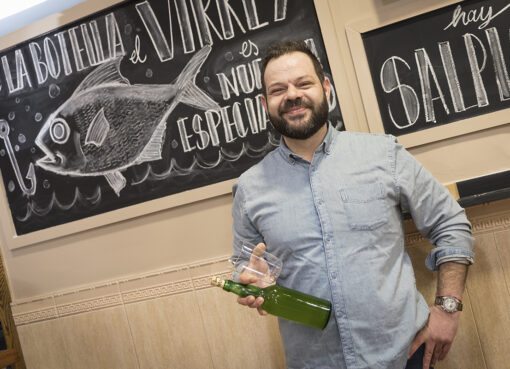 Pablo Fernández sonriendo con botella de sidre frente a pizarra con dibuxu de pexe nel chigre La Botella n’Avilés