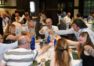 Un grupo de personas brinda con copas de sidra alrededor de una mesa.